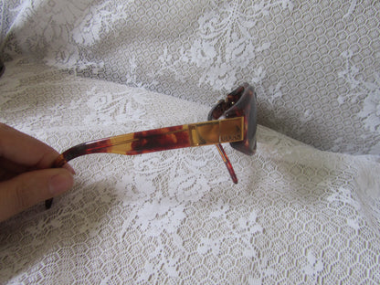 Sunglasses with a tortoiseshell frame held over a textured white surface