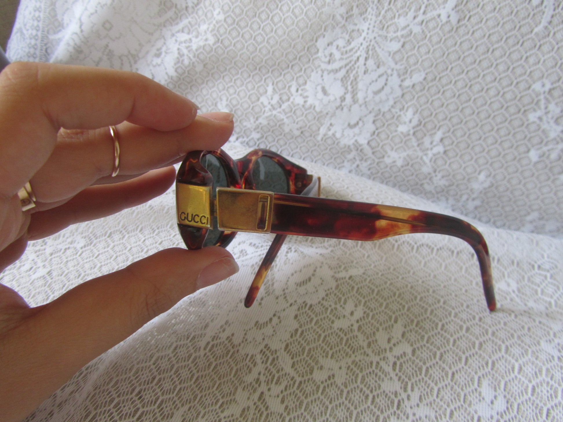 Sunglasses with a Gucci case held by a hand on a textured white background