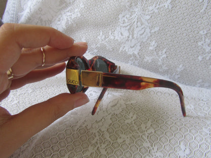 Sunglasses with a Gucci case held by a hand on a textured white background