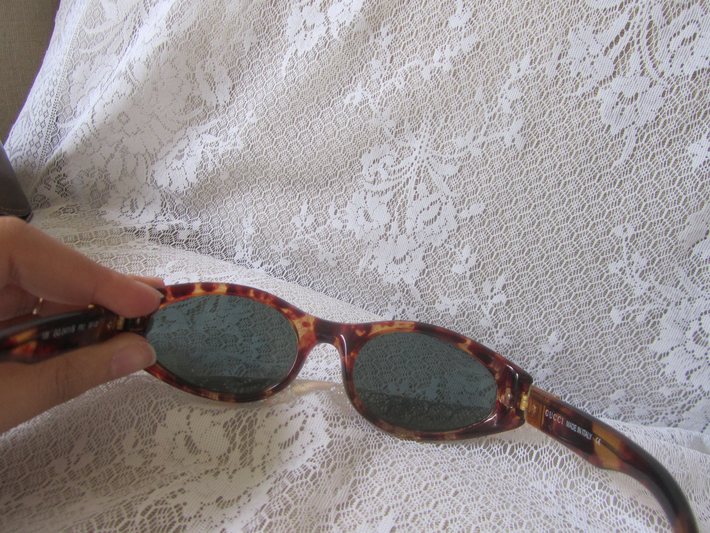 Sunglasses with tortoiseshell frame held over a white lace fabric background