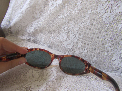 Sunglasses with tortoiseshell frame held over a white lace fabric background