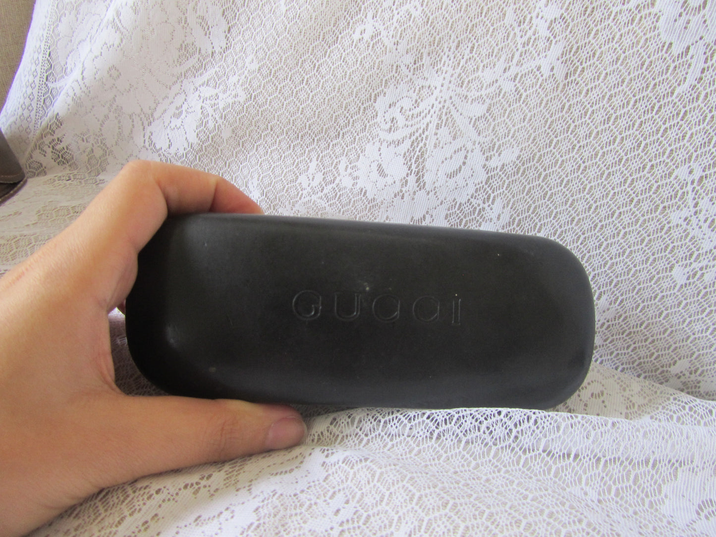 Black Gucci sunglasses case held by a hand on a textured white surface