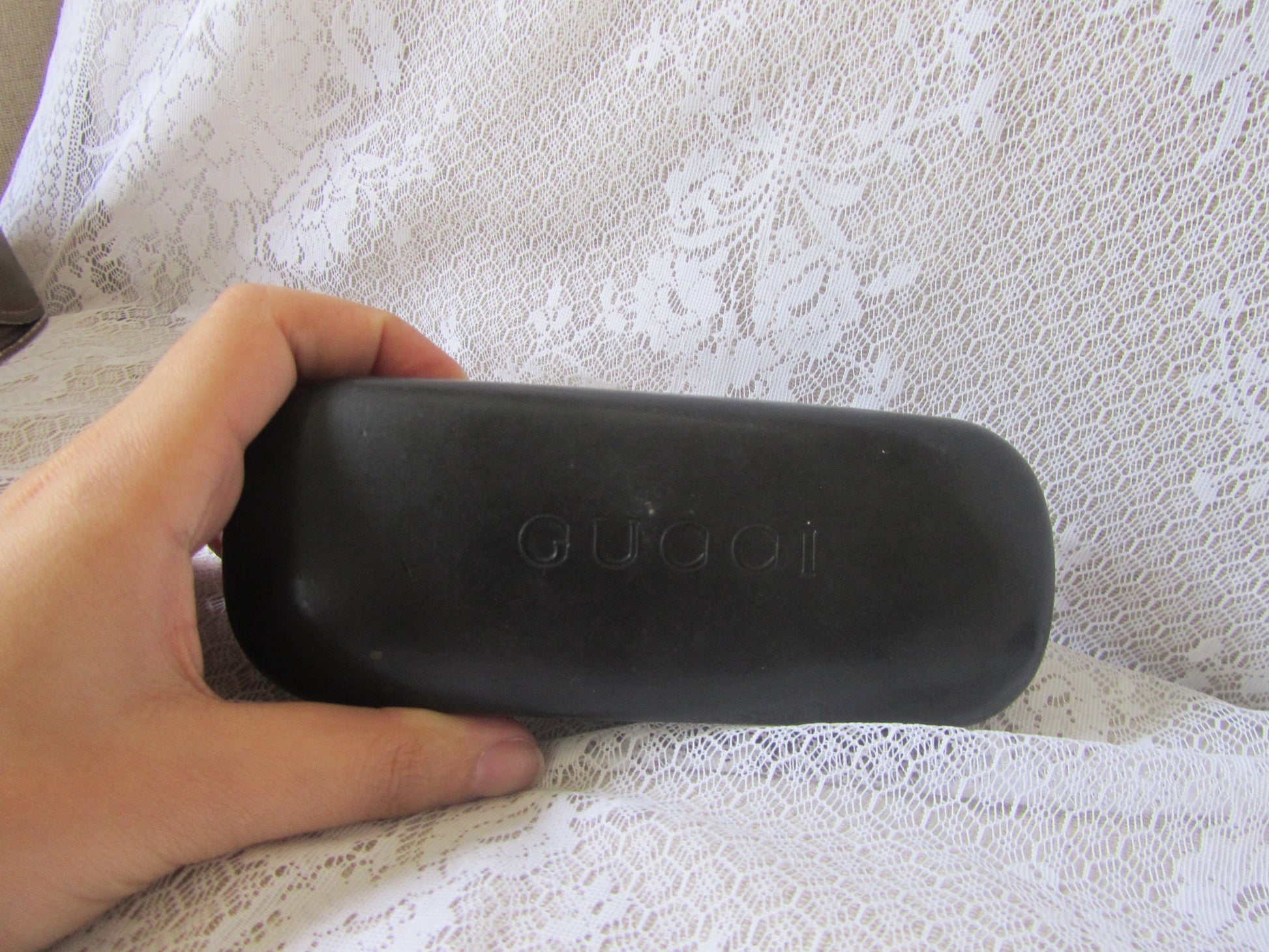 Black Gucci sunglasses case held by a hand on a textured white surface