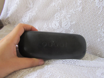 Black Gucci sunglasses case held by a hand on a textured white surface