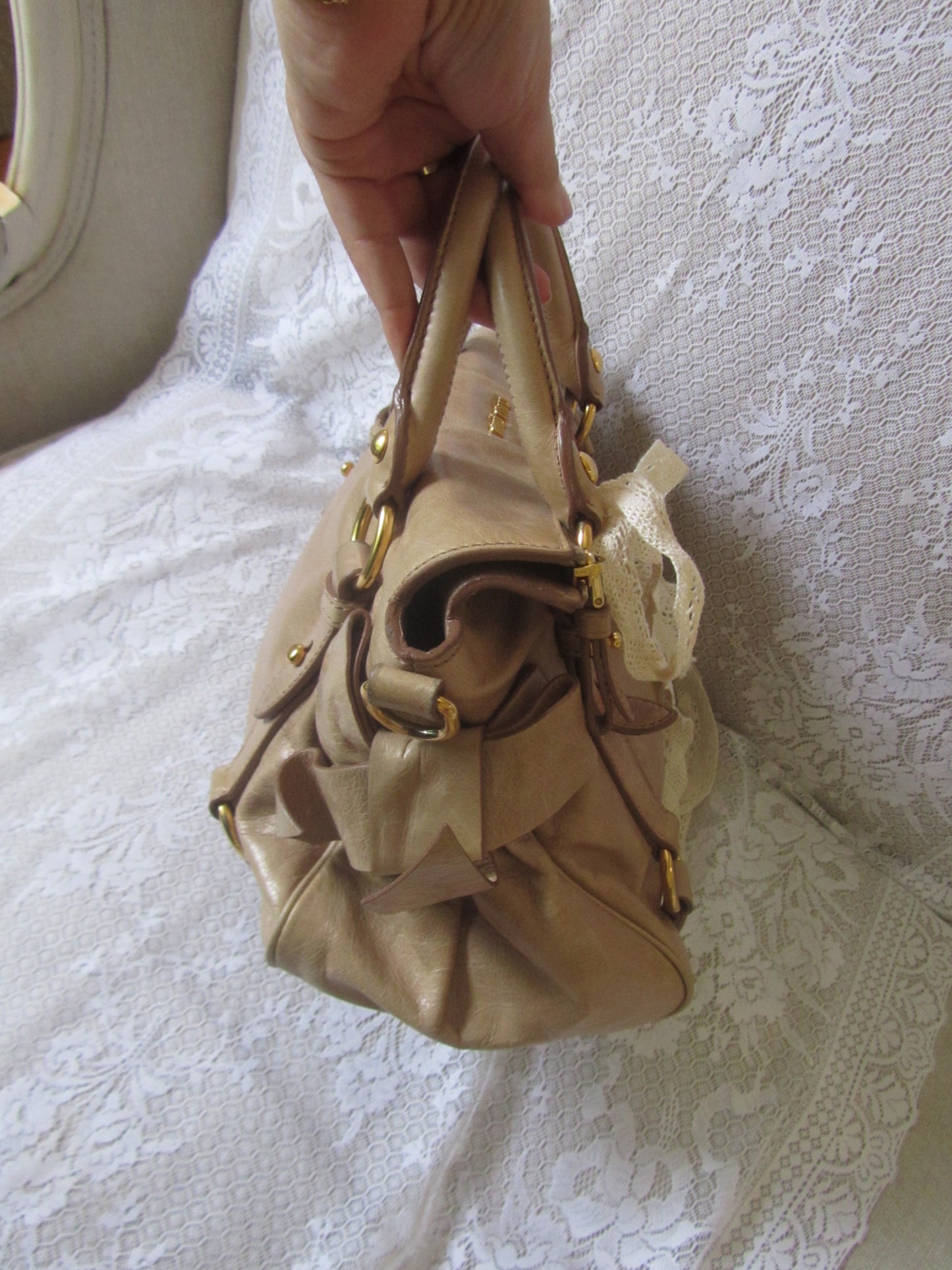 Gold handbag held by a hand on a white lace background
