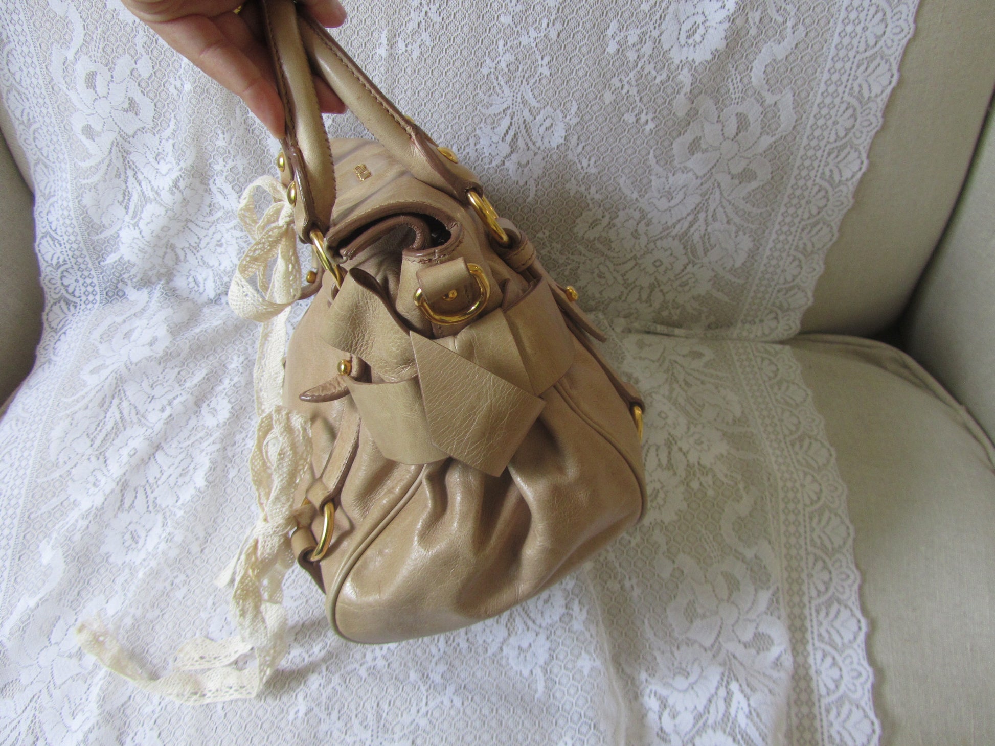 Beige handbag held by a hand on a white lace background