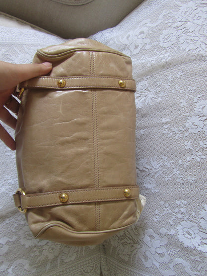Beige handbag with gold accents held by a hand on a textured white background
