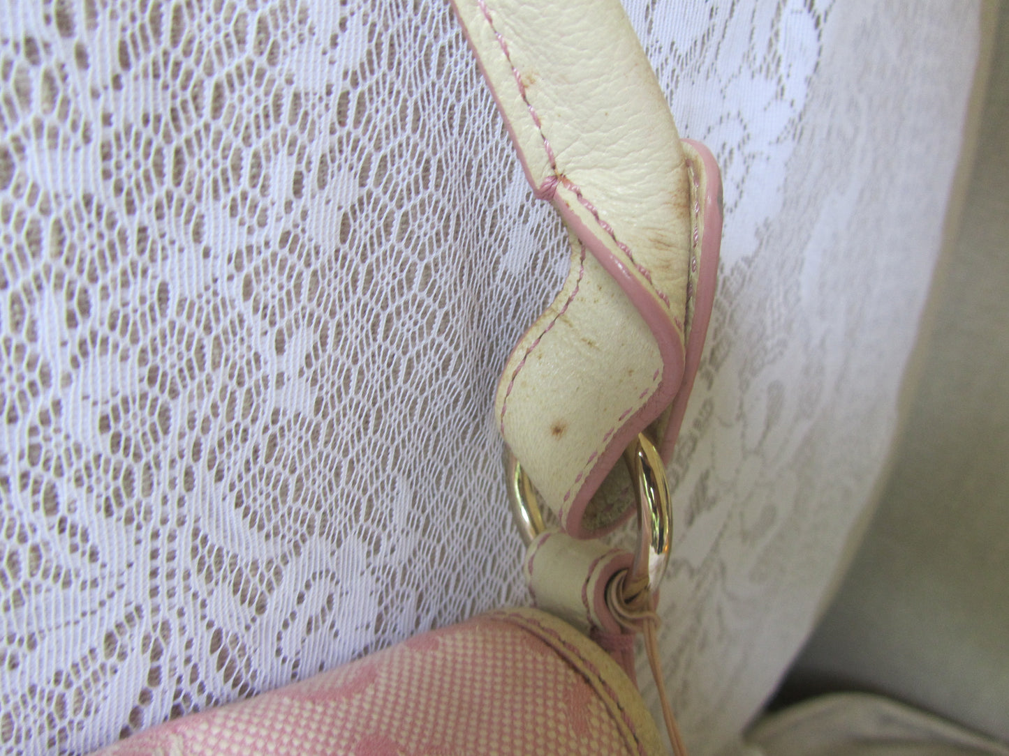 Close-up of a beige handbag handle with gold hardware against a textured white background
