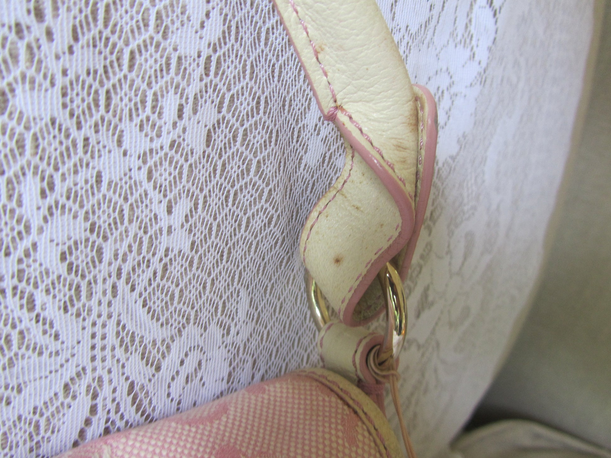 Close-up of a beige handbag handle with gold hardware against a textured white background