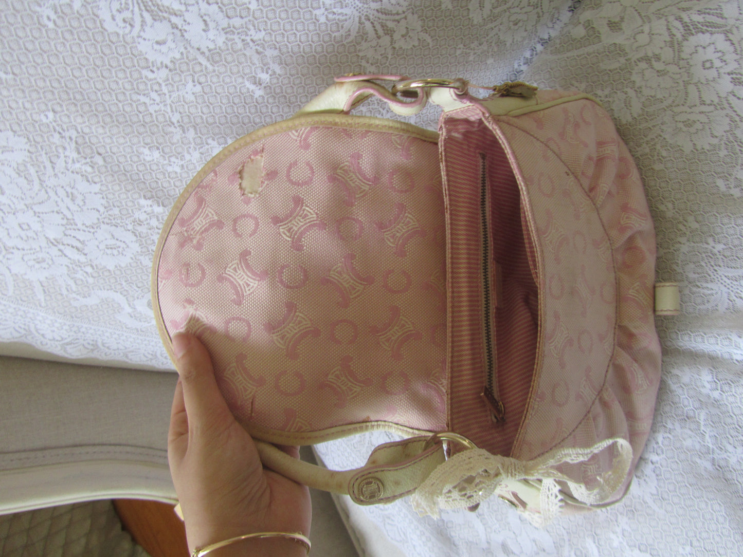 Pink handbag with lace details held by a hand against a textured white background