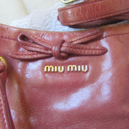 pink leather handbag with 'miu miu' logo on a beige background