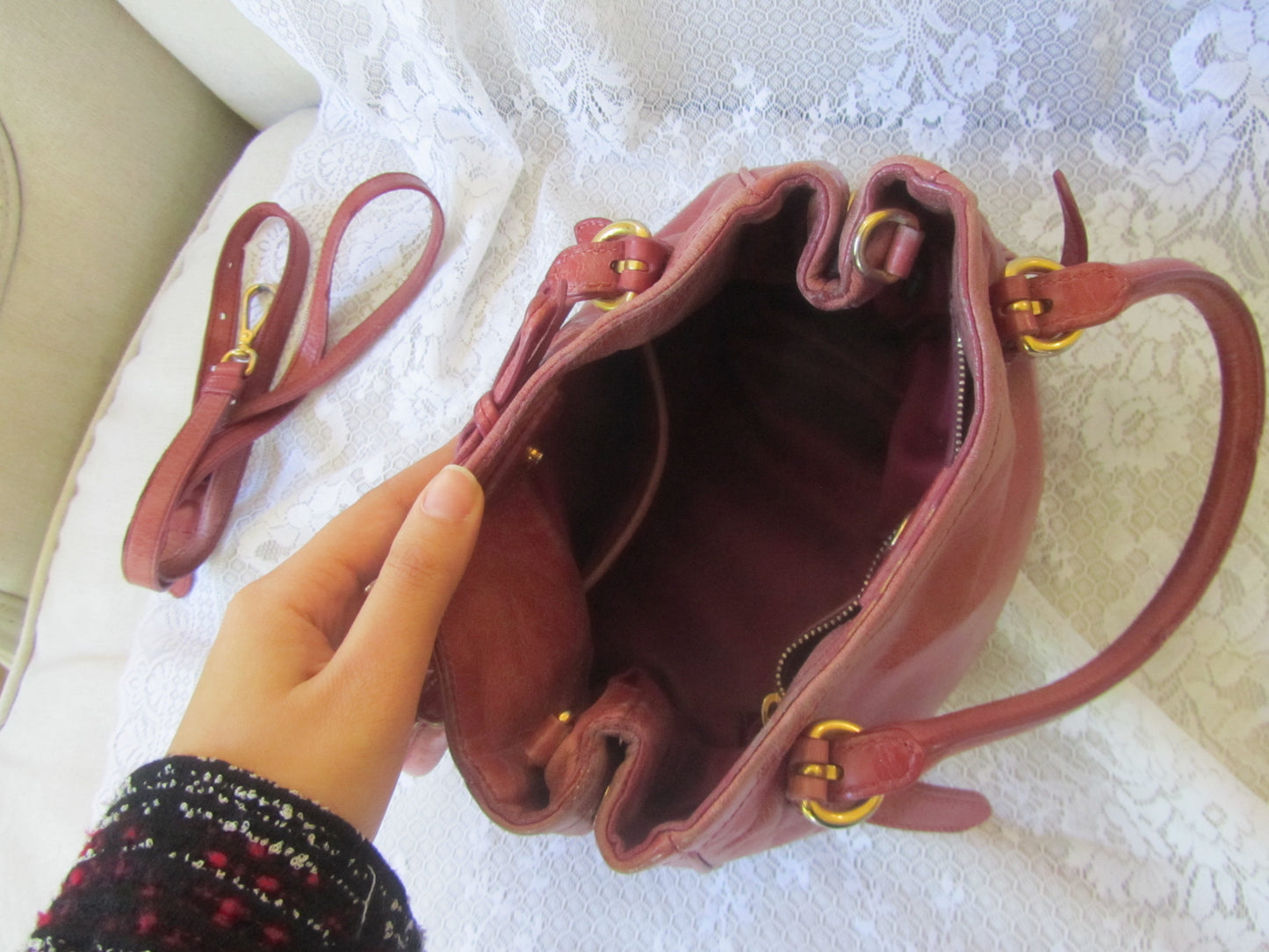 Hand holding a maroon handbag with gold hardware on a textured surface