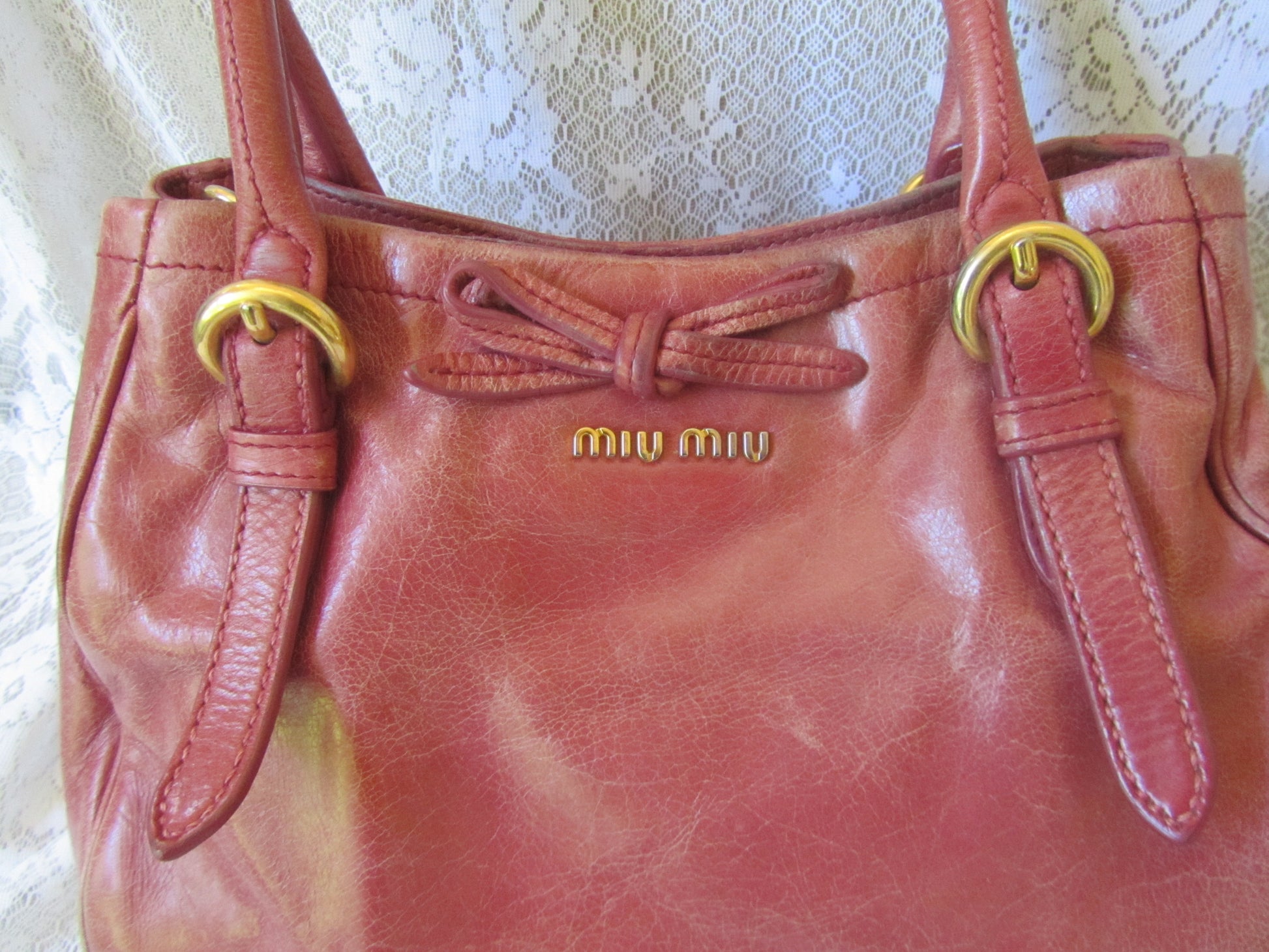 Pink handbag with gold accents and 'Miu Miu' logo on a textured white background