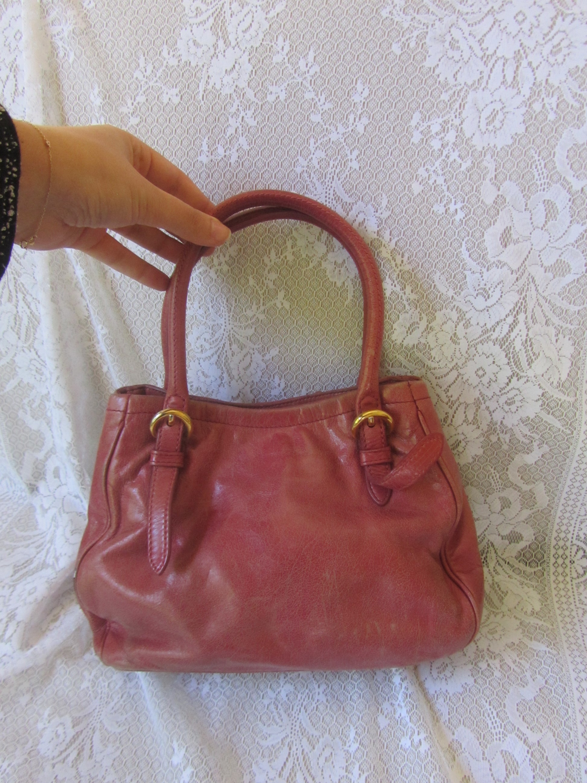 Red handbag held by a hand on a textured white background