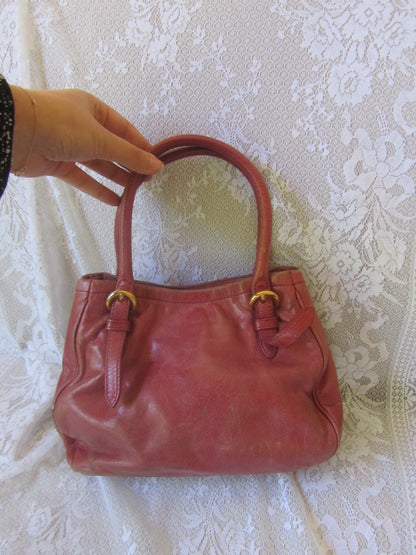Red handbag held by a hand on a textured white background