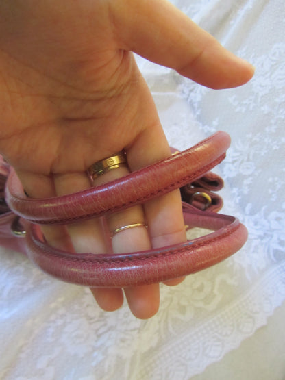 Pink leather strap held in a hand against a white textured background