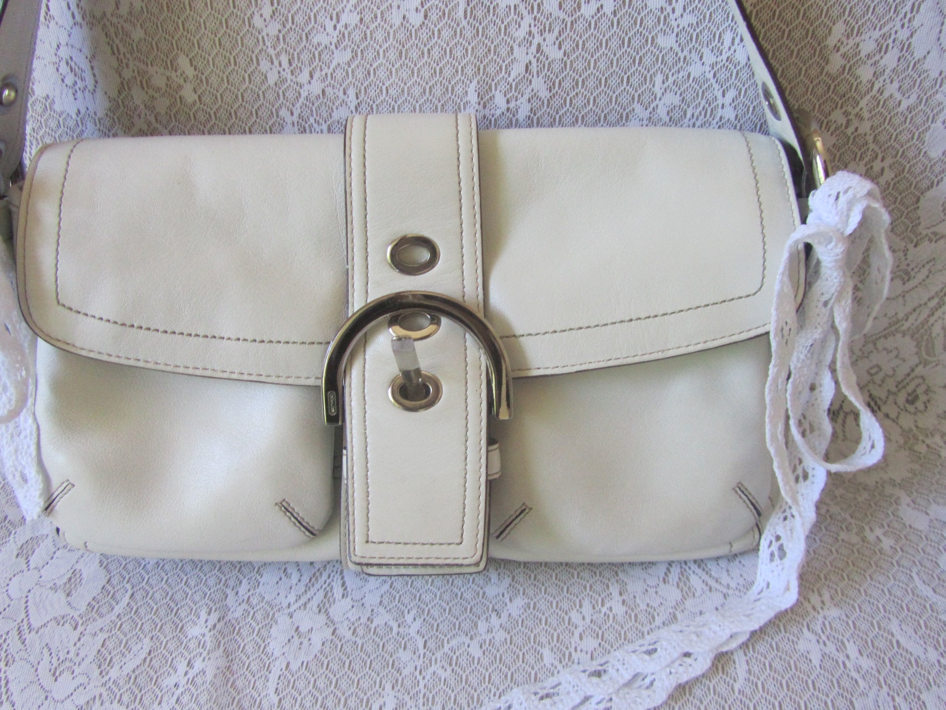 White handbag with a decorative strap on a lace background