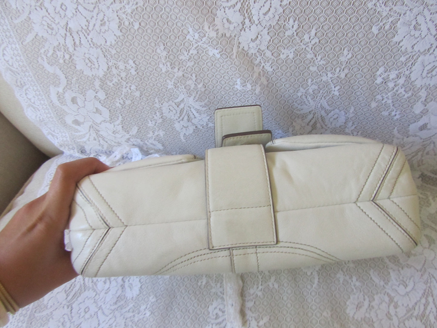 White quilted handbag held by a hand on a textured white surface