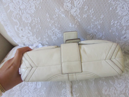 White quilted handbag held by a hand on a textured white surface