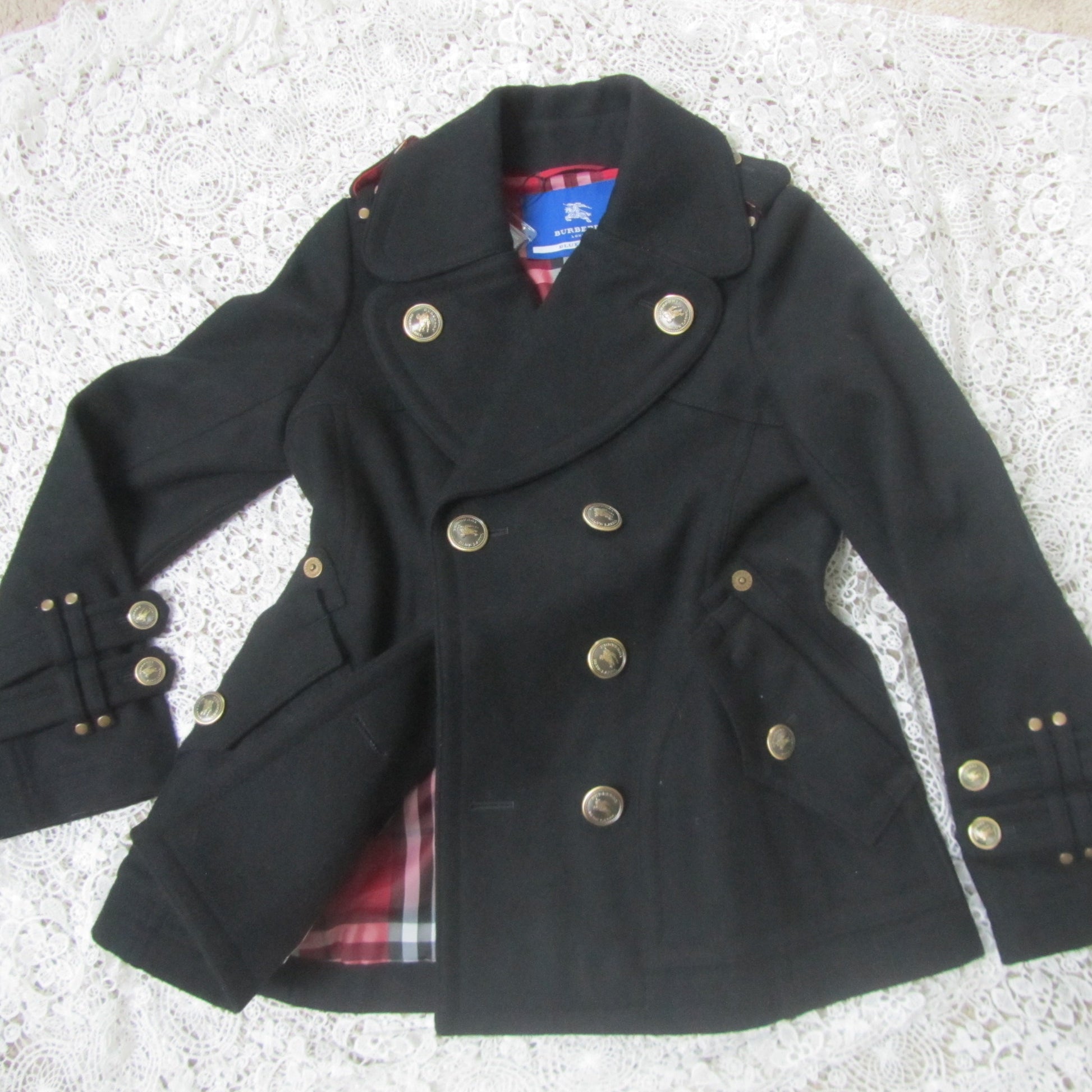 black peacoat with red plaid interior and golden buttons on a lace background
