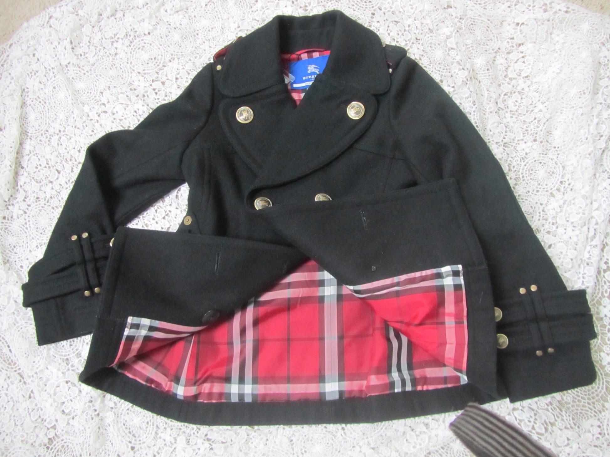 black peacoat with red plaid interior and golden buttons on a lace background