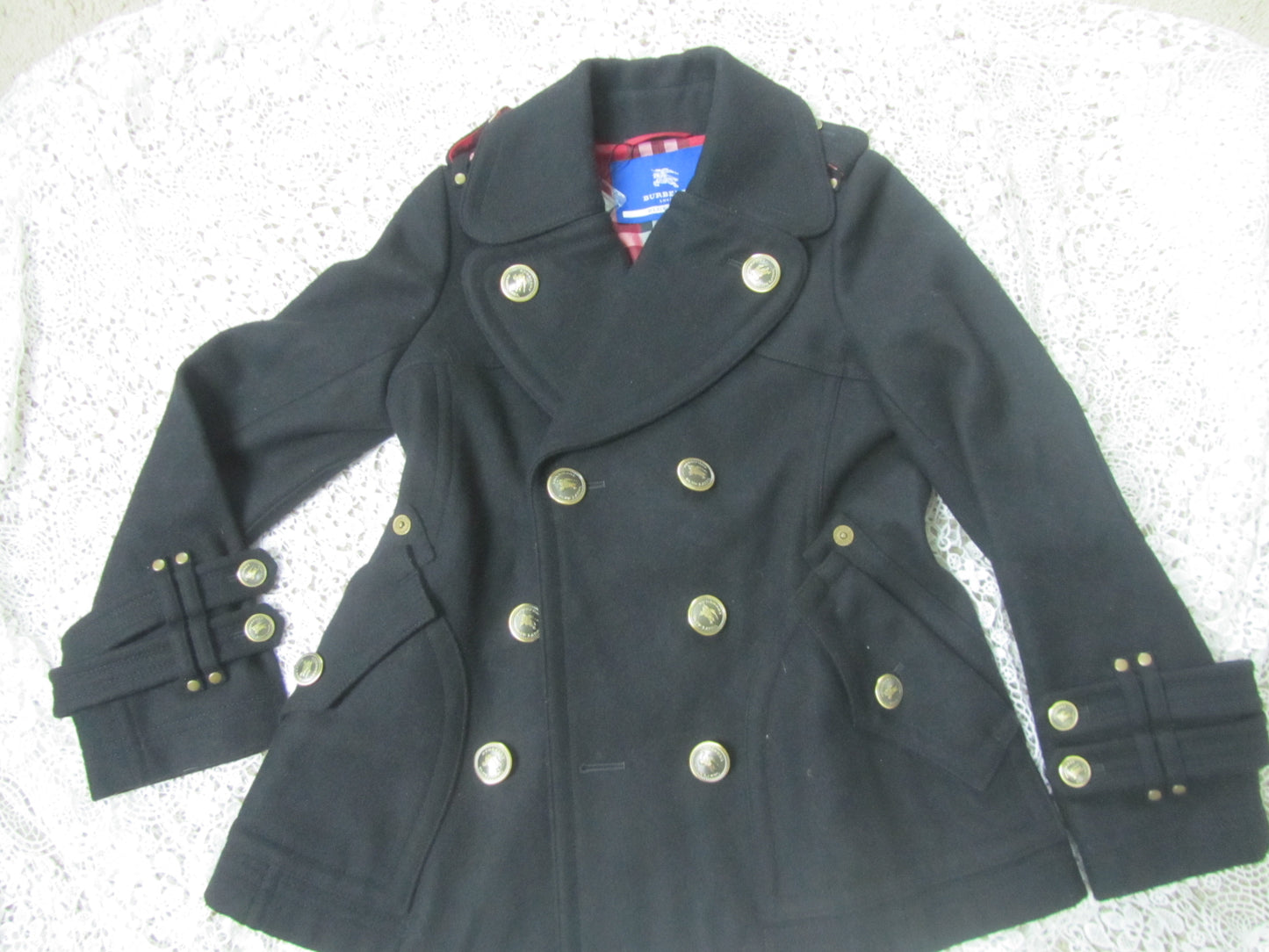 black peacoat with red plaid interior and golden buttons on a lace background