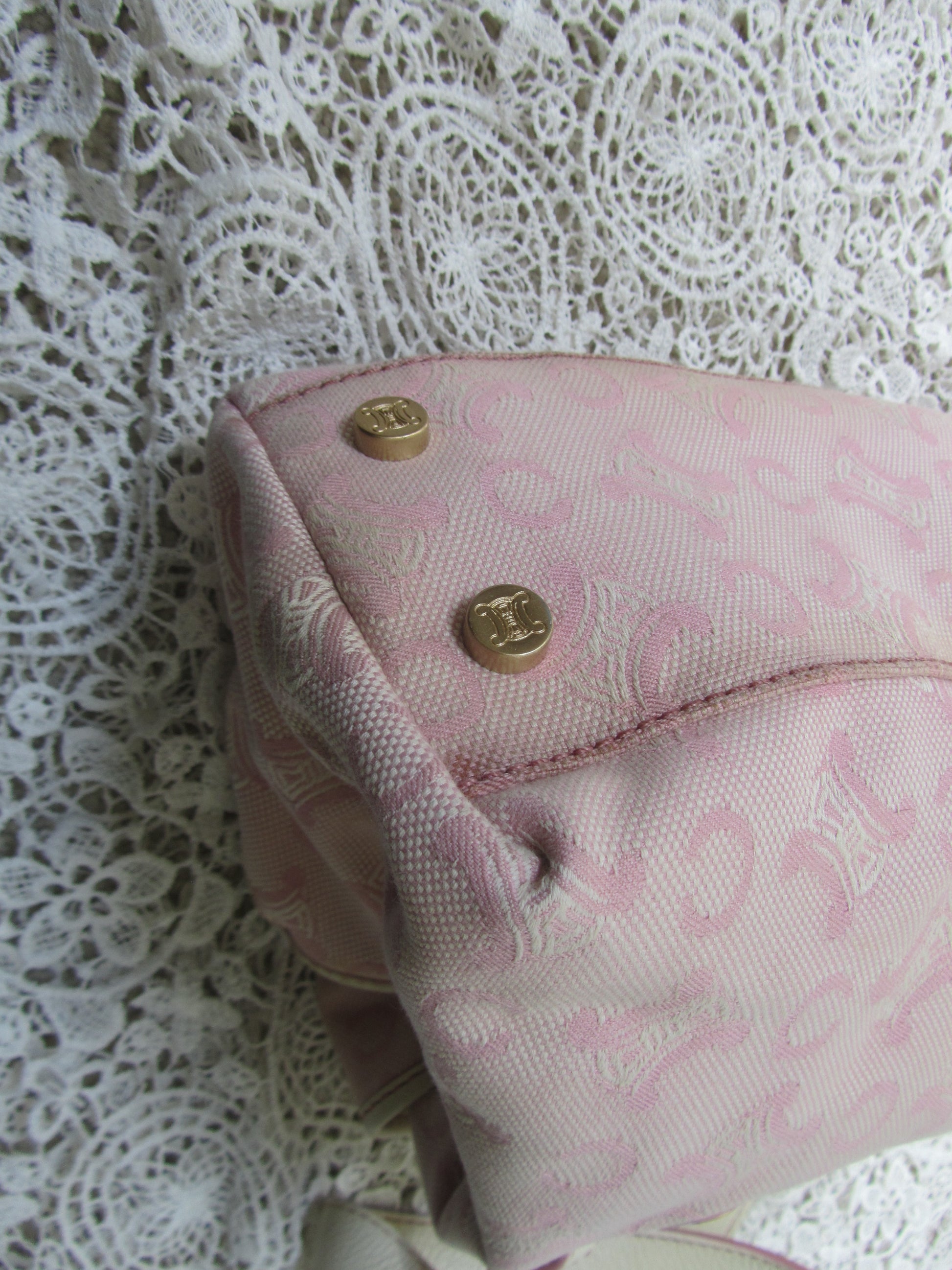 the corner of a pink celine bag with  gold details on a lace background  