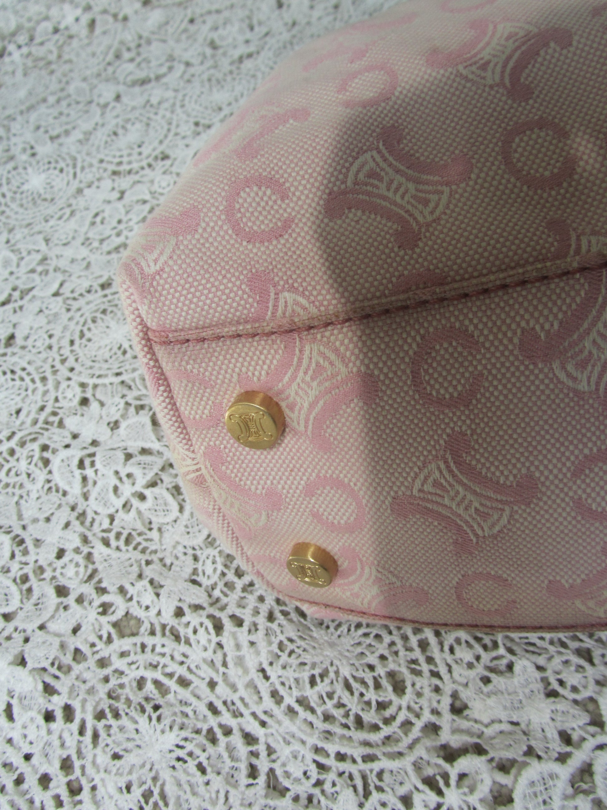the corner of a pink celine bag with  gold details on a lace background  