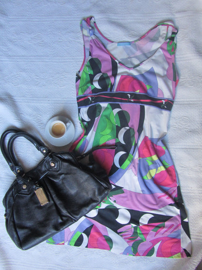 Black handbag on a colorful patterned fabric with a small cup of coffee in the background.