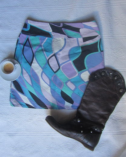 Folded colorful skirt with abstract patterns next to a black glove on a light surface.