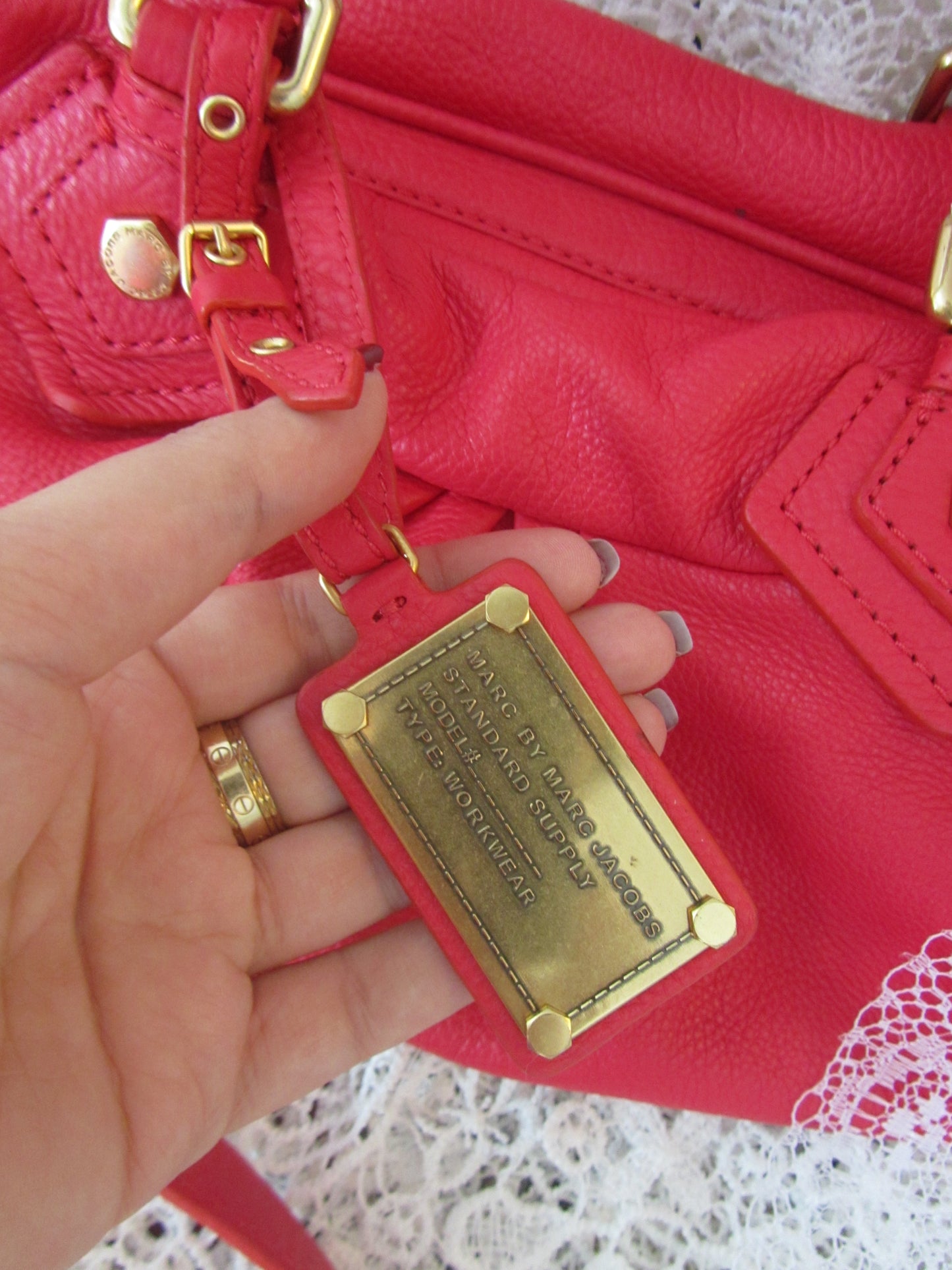 Red handbag with gold plaque held by a hand on a white lace background