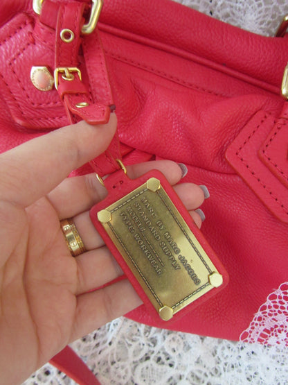 Red handbag with gold plaque held by a hand on a white lace background