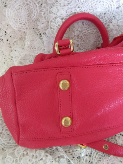 Red leather handbag with gold accents on a textured white surface