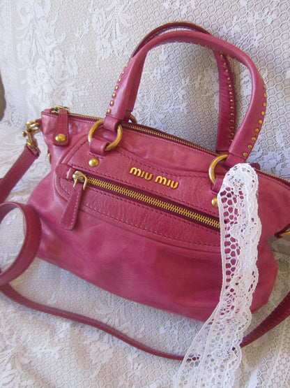 Pink handbag with gold accents on a textured white surface