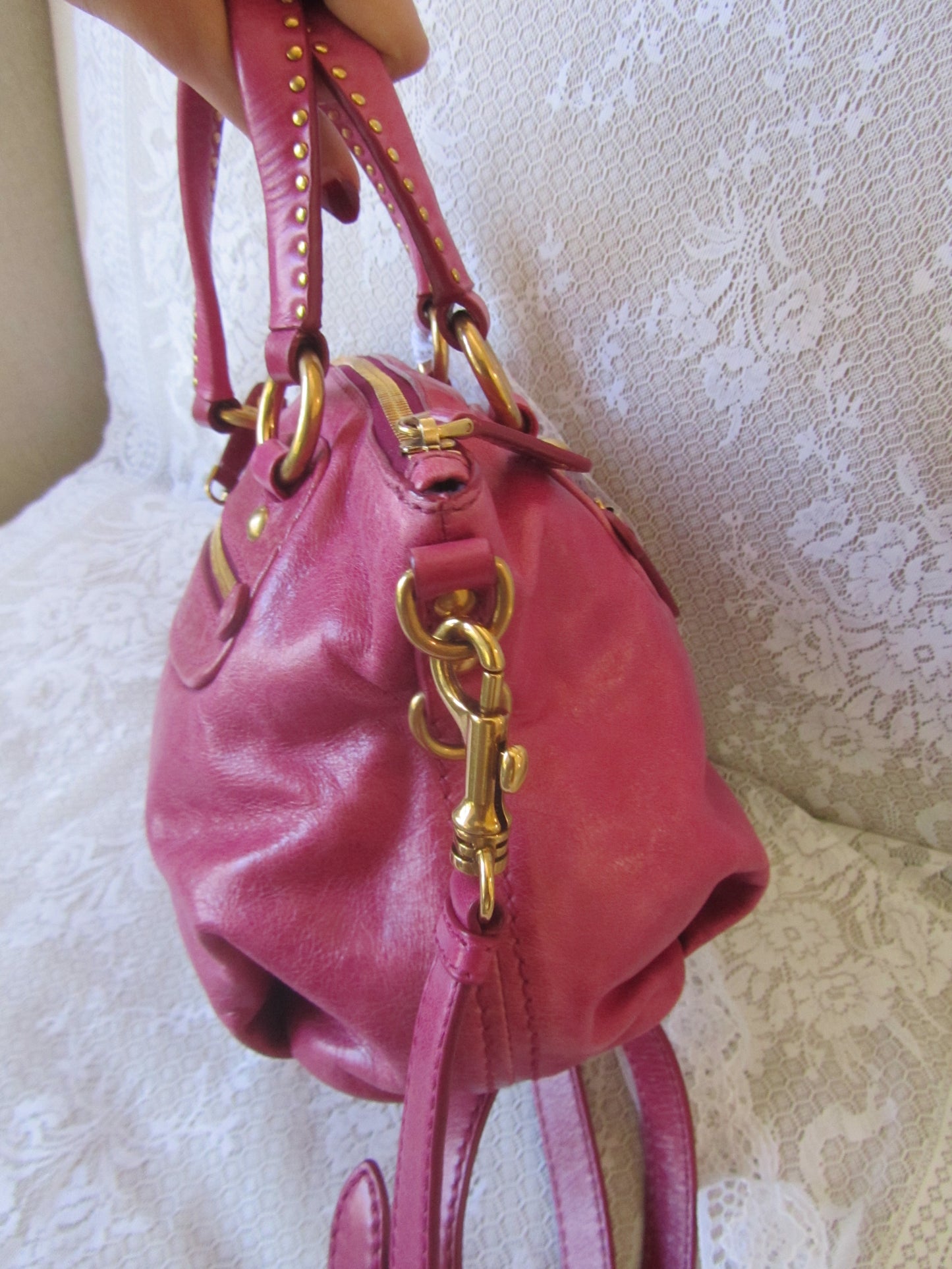 Pink handbag with gold chain detail held against a textured white background