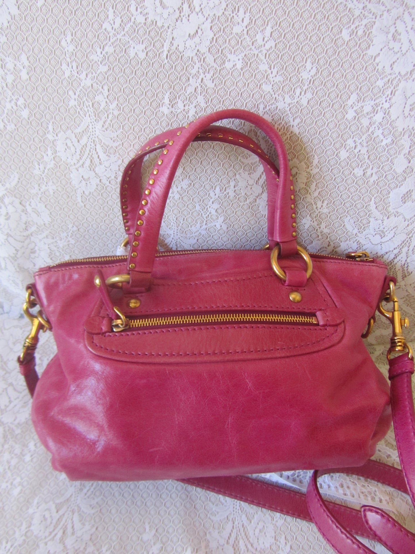 Pink handbag with gold accents on a textured white surface
