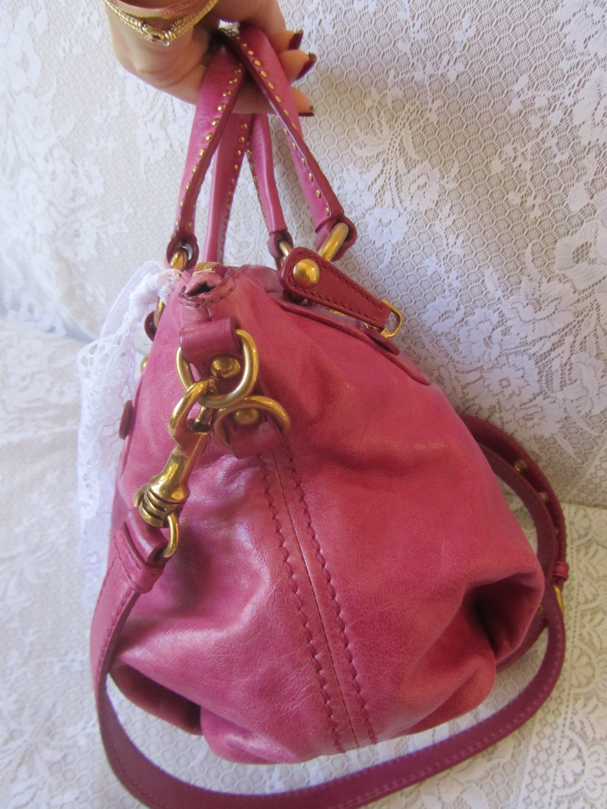 Pink handbag with gold accents held by a hand on a textured white background