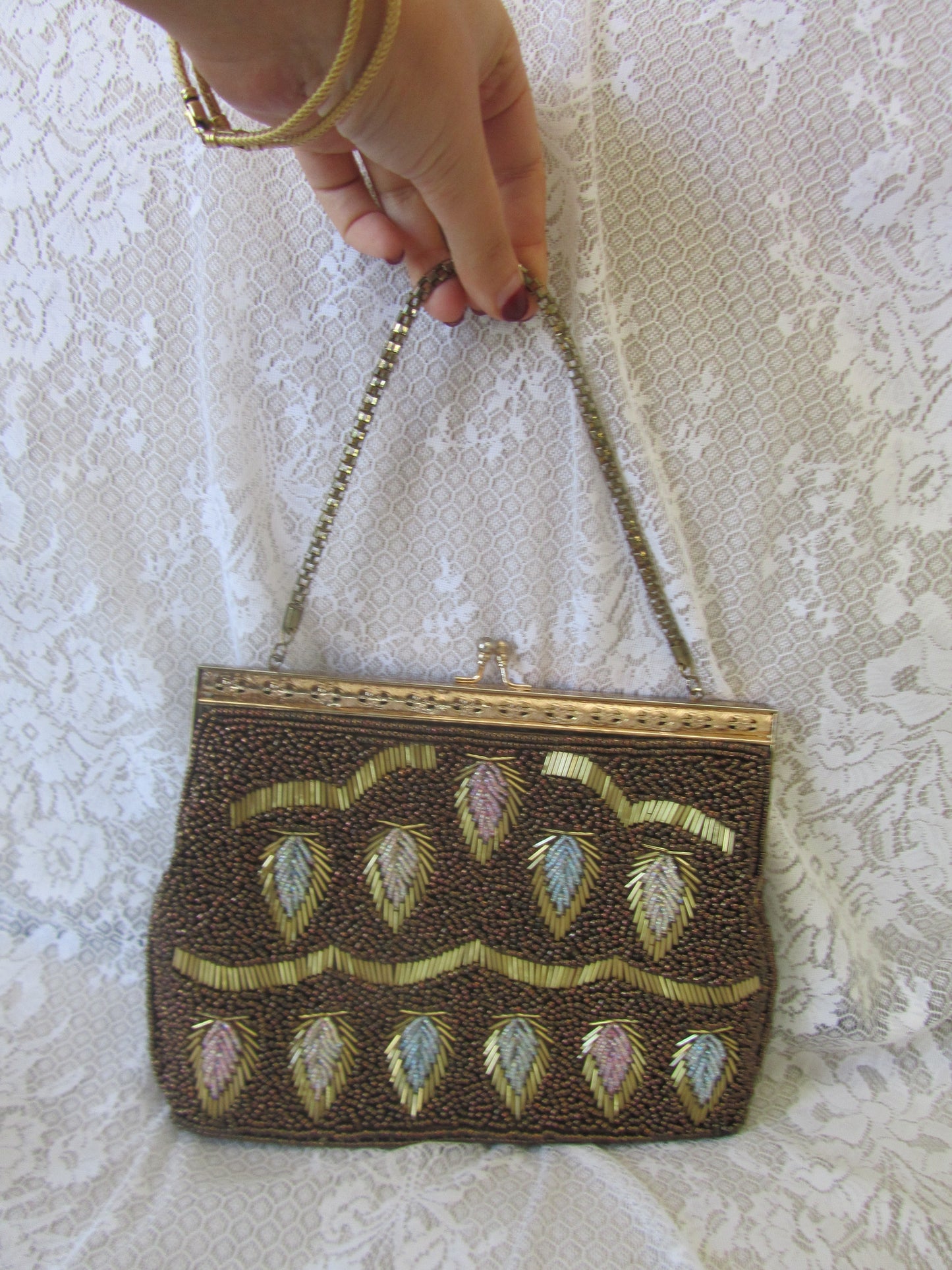 Hand holding a beaded clutch bag with intricate designs on a lace background