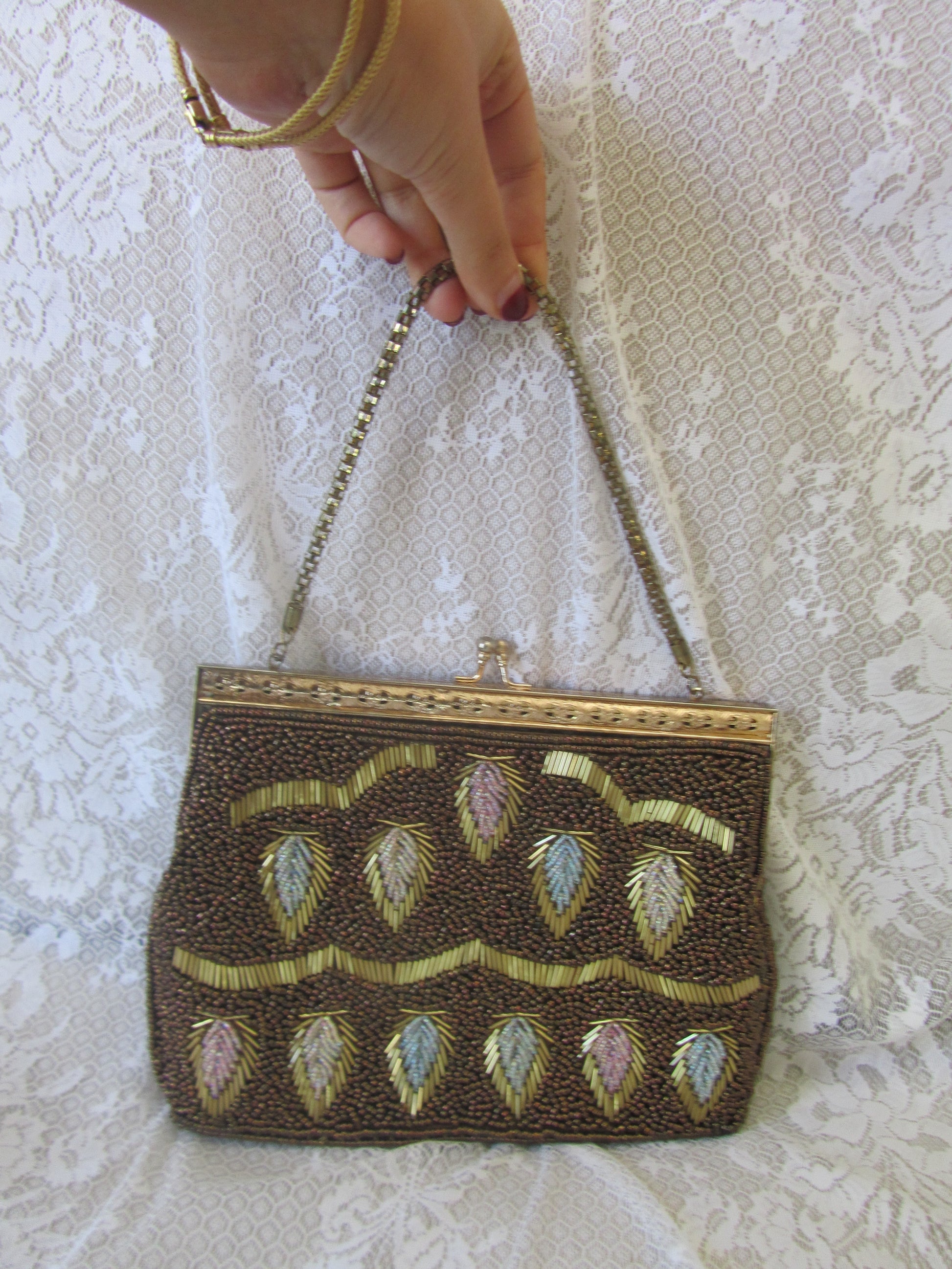 Hand holding a beaded clutch bag with intricate designs on a lace background