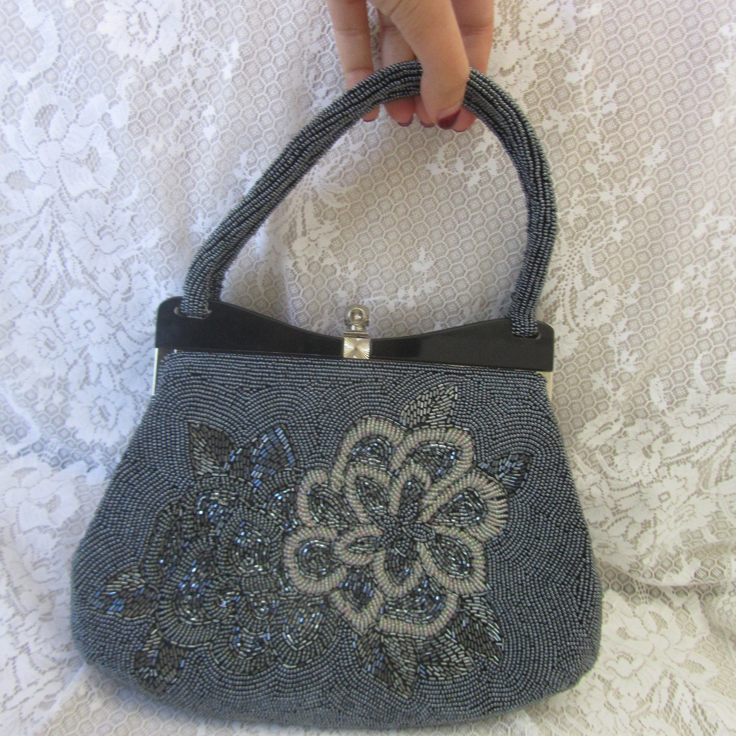 Gray handbag with floral design held by a hand on a textured white surface