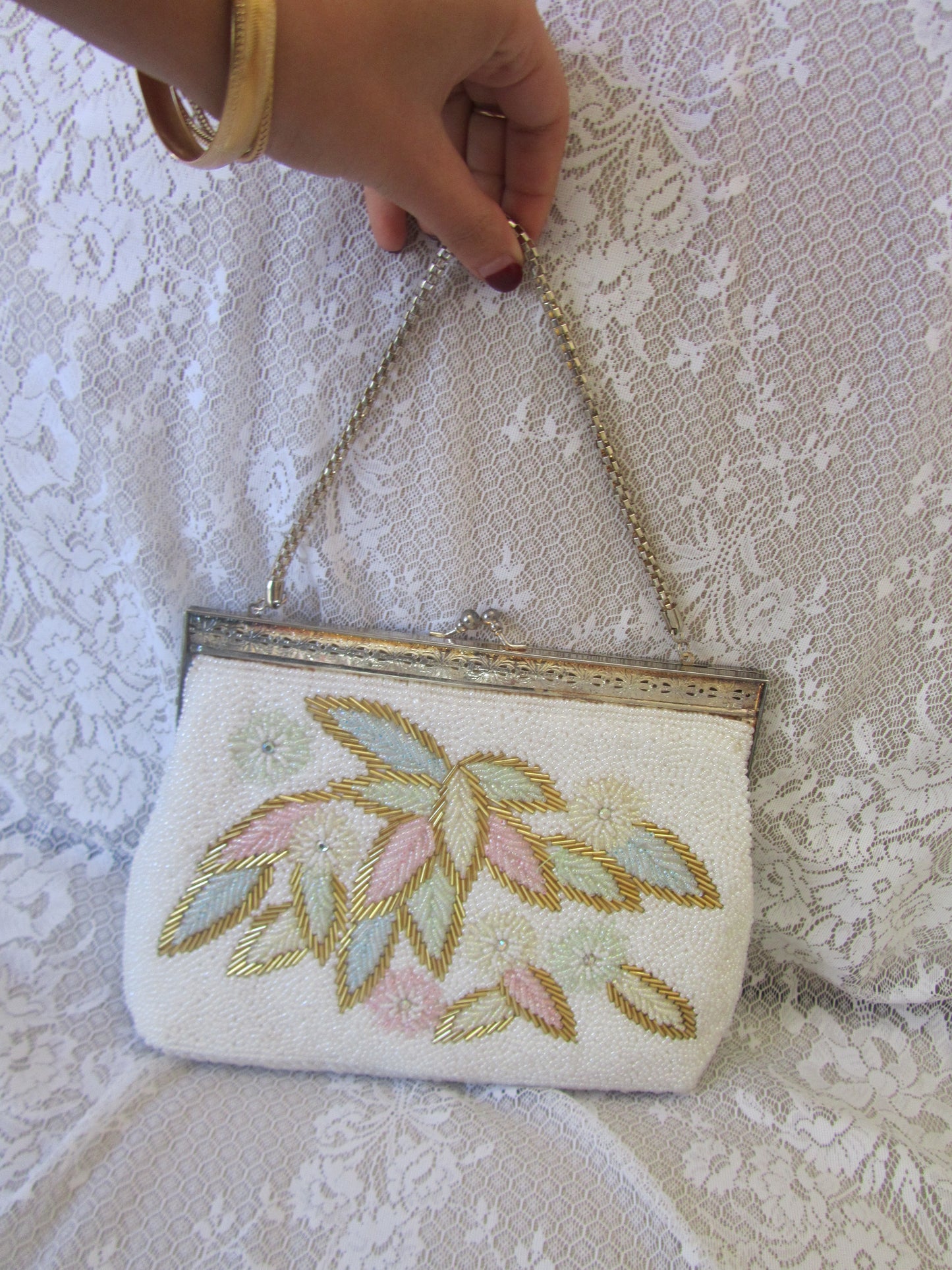 Hand holding a small embroidered clutch bag on a lace background
