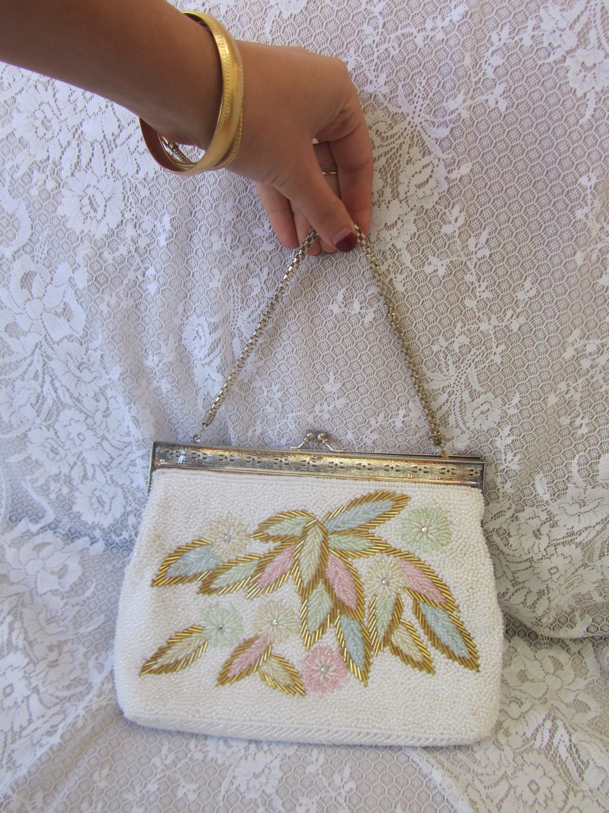 Hand holding a white clutch with floral embroidery on a textured surface