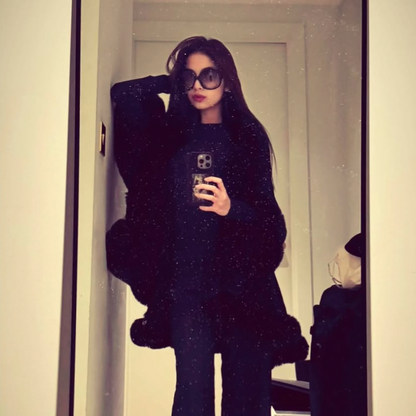 Person wearing a black outfit with a fluffy coat in front of a mirror.