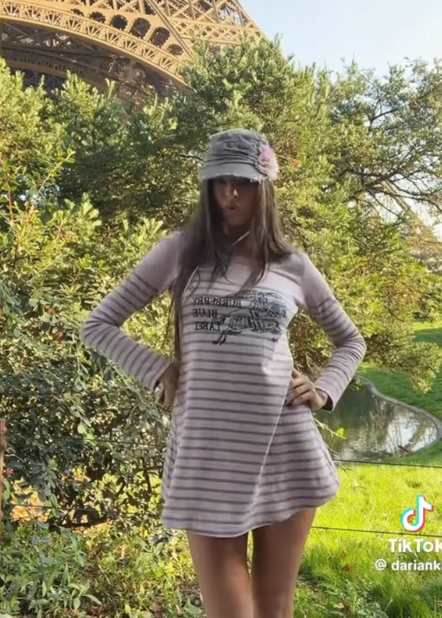 Woman posing in front of the Eiffel Tower with trees and grass in the background