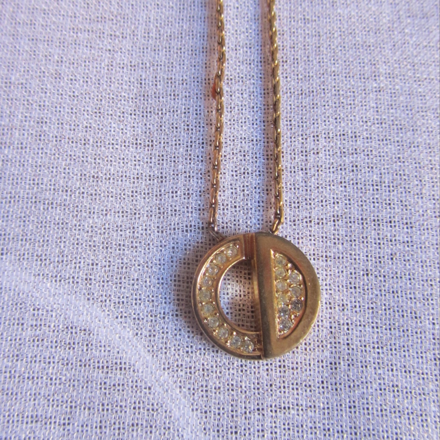 Gold necklace with a round pendant on a light fabric background