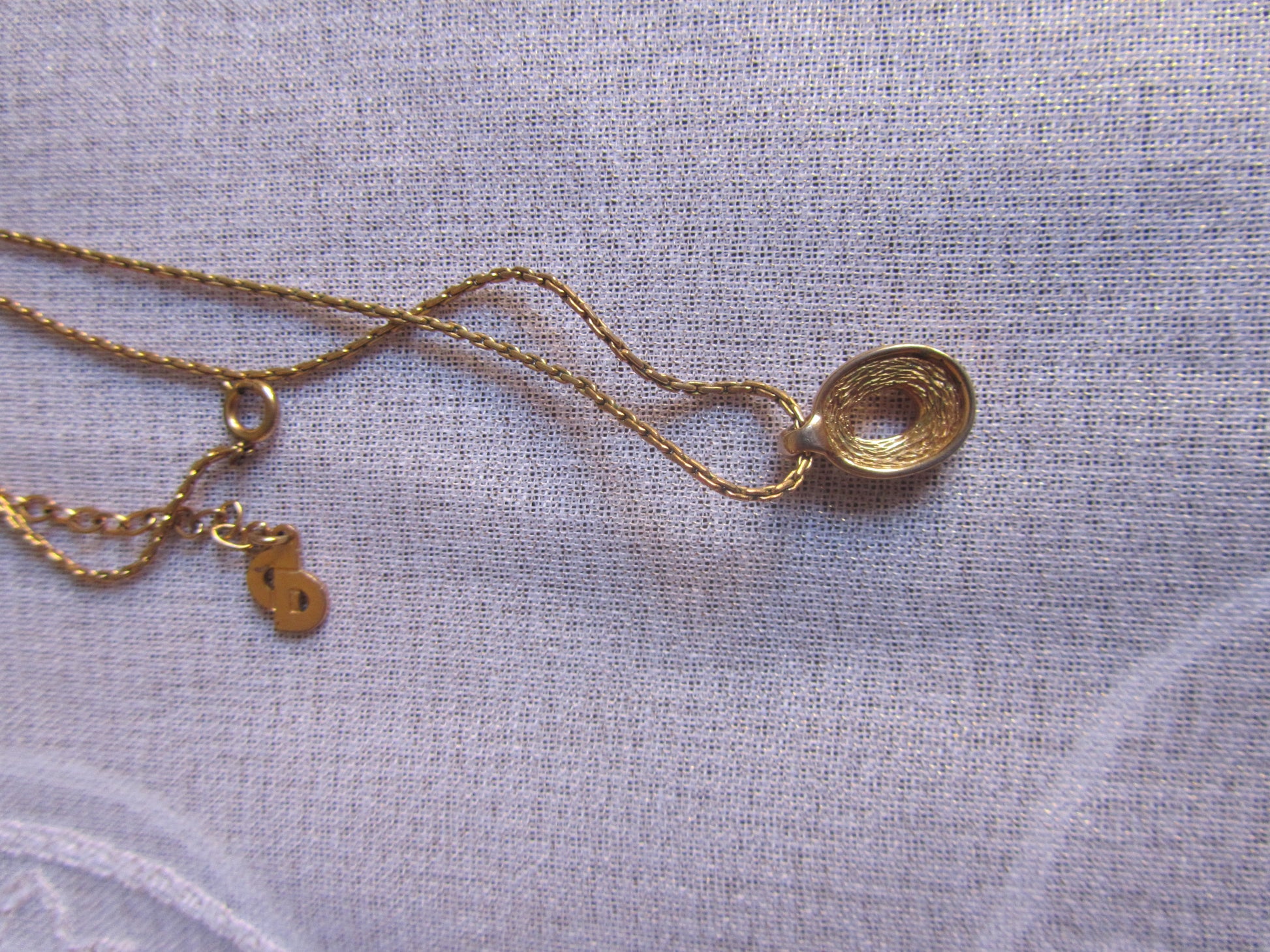 Gold necklace with a pendant on a light gray fabric background