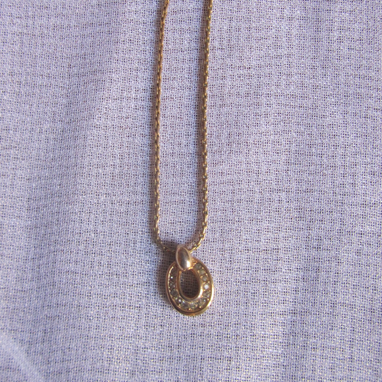 Gold necklace with a heart-shaped pendant on a light blue fabric background