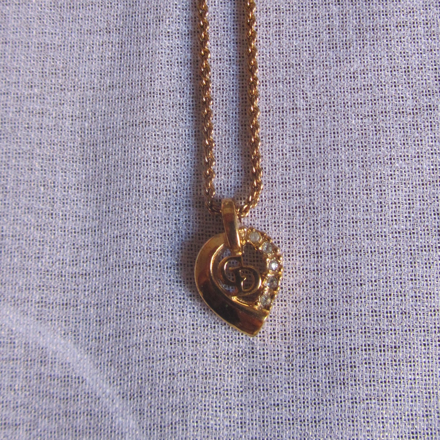 Gold necklace with a heart-shaped pendant on a light blue fabric background