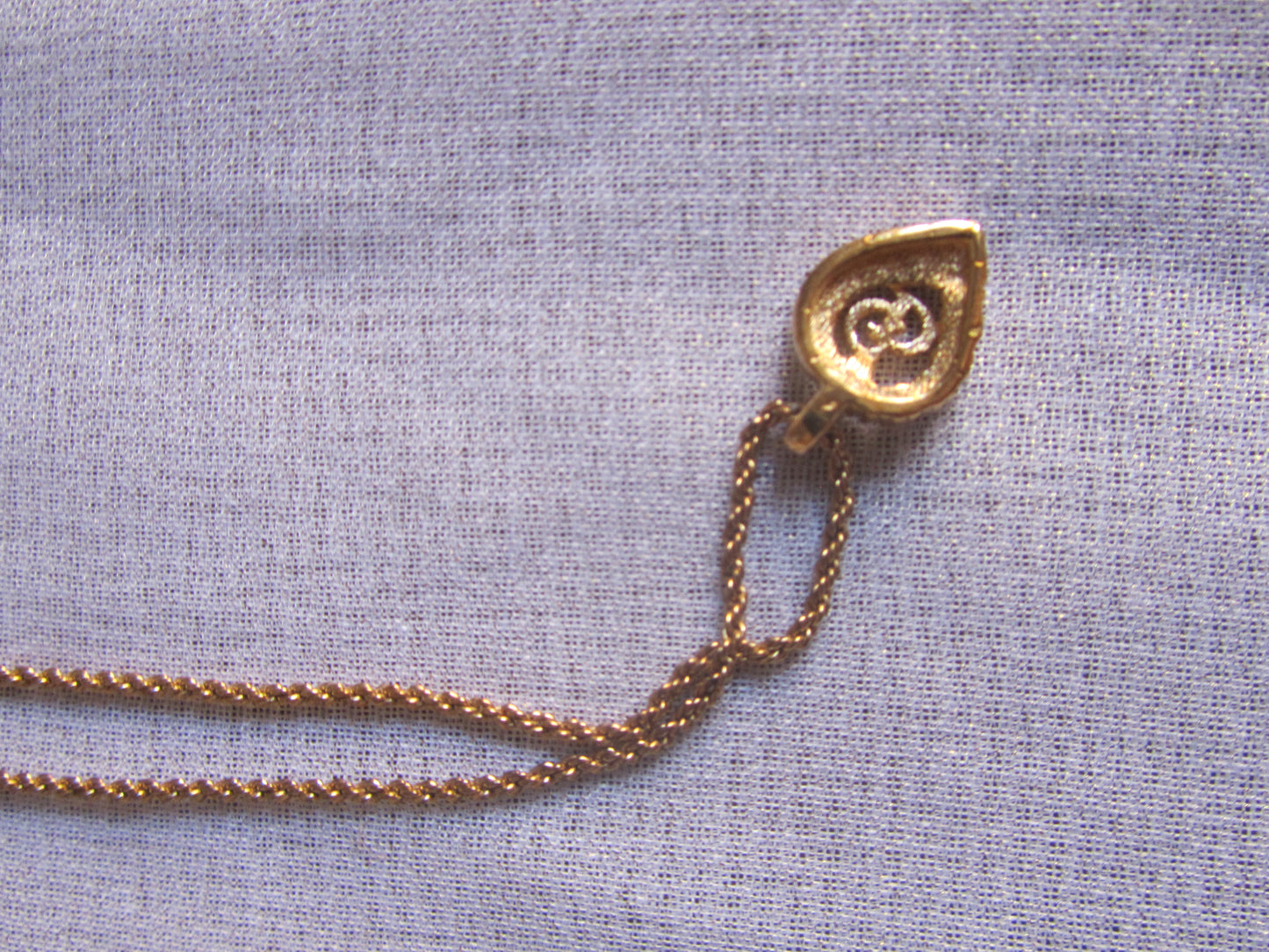 Gold necklace with a pendant on a light blue fabric background