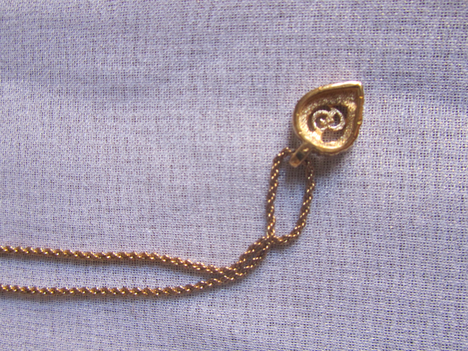 Gold necklace with a pendant on a light blue fabric background